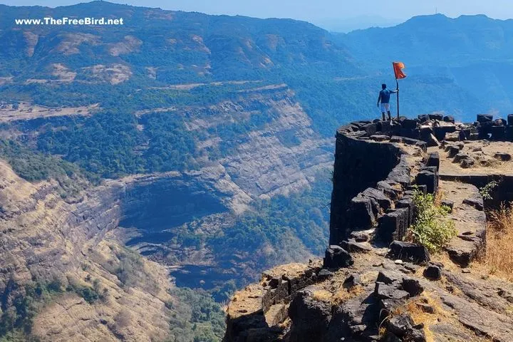 A trekker holding a saffron flag on the high ramparts of Rajmachi Fort above a deep monsoon valley