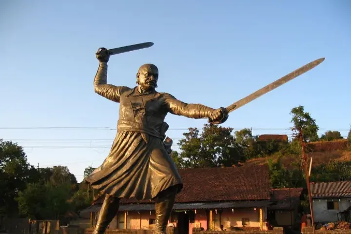 Bronze statue of Baji Prabhu Deshpande holding two swords against a clear blue sky at Panhala Fort