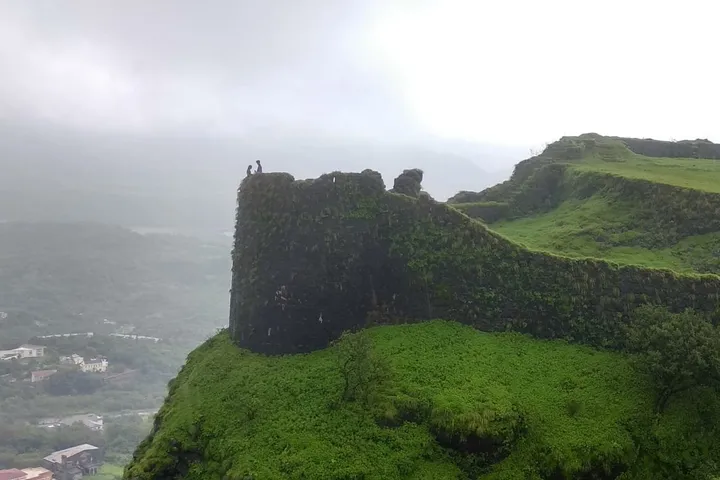 A moss-covered stone bastion of Korigad Fort jutting from a green cliffside under a misty sky